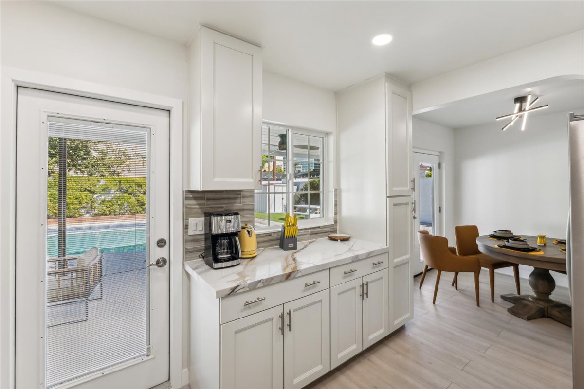 Kitchen with white cabinets, marble counters, backyard pool view, and dining area.