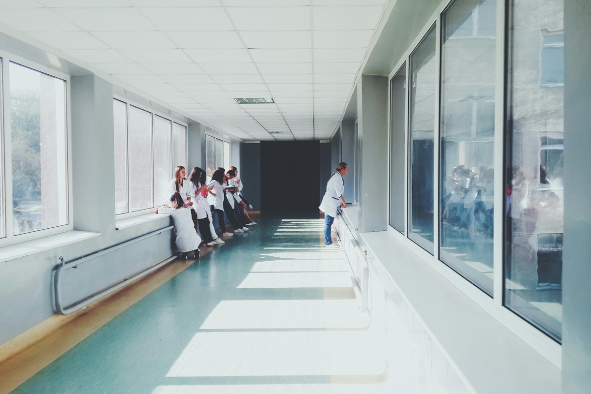 Group of medical professionals in white coats standing in a bright hospital hallway.
