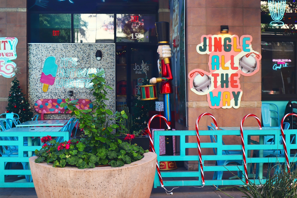 Outdoor seating area at Jojo's Shake Bar, decorated with a nutcracker, candy canes, small Christmas trees, and a “Jingle All The Way” sign.