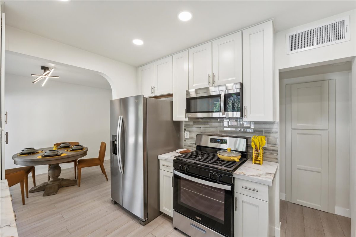 Modern kitchen with stainless appliances, tiled backsplash, white cabinets, and nearby dining table.