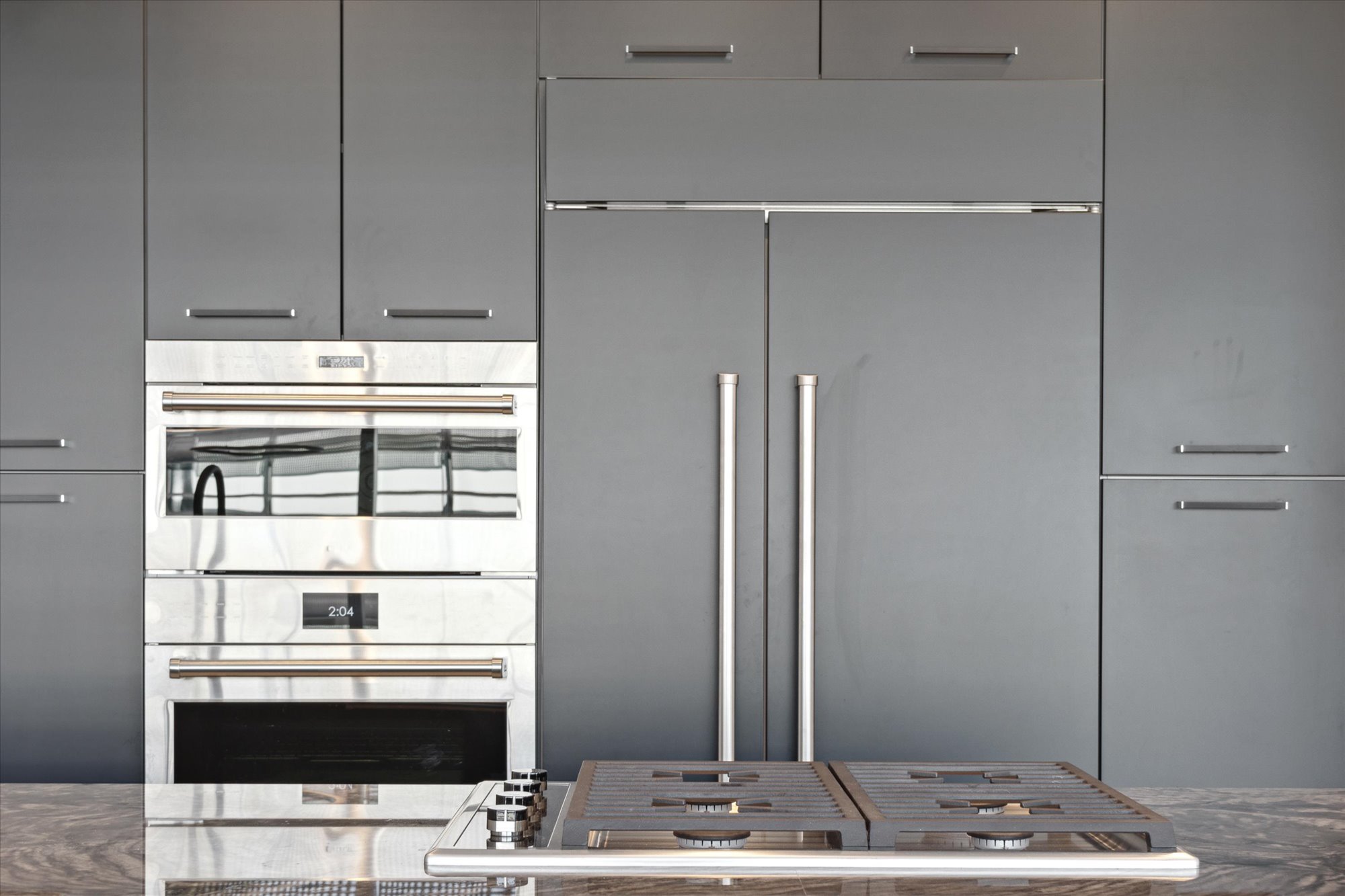 A sleek, modern kitchen with built-in stainless steel appliances, a double-door refrigerator, and minimalist gray cabinetry.