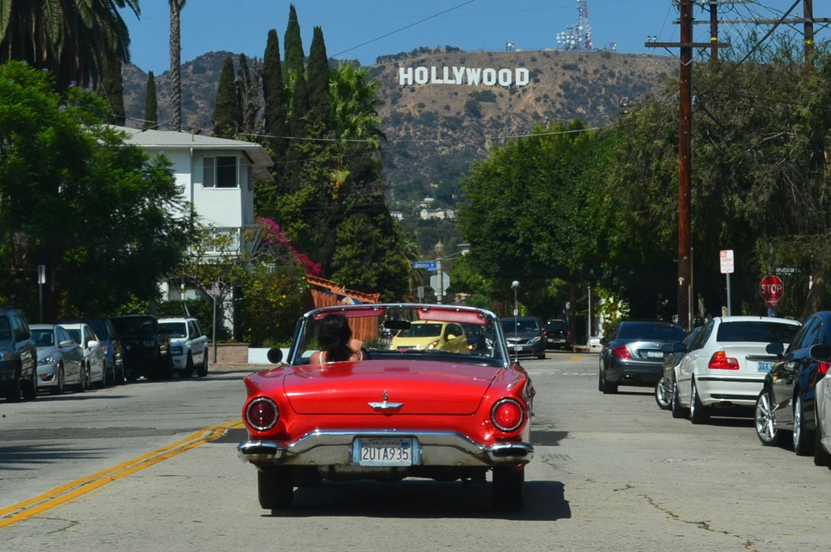  A classic red convertible driving toward the Hollywood sign on a sunny street in Los Angeles.