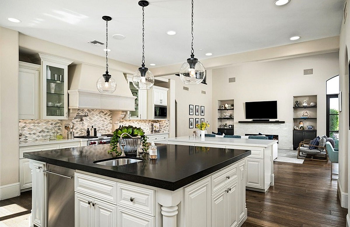 Luxury kitchen with white cabinetry, a large black island, and open view into the family room.