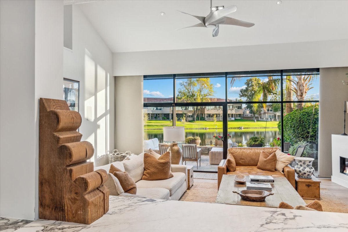 A bright, airy living room with large windows showcasing a serene waterfront and lush greenery.
