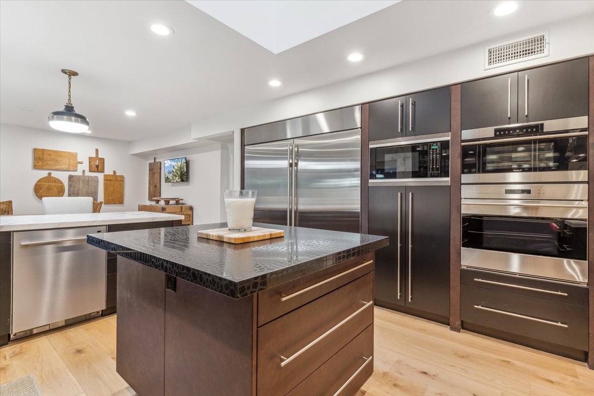 A contemporary kitchen featuring dark cabinetry, stainless steel appliances, and a textured island countertop.