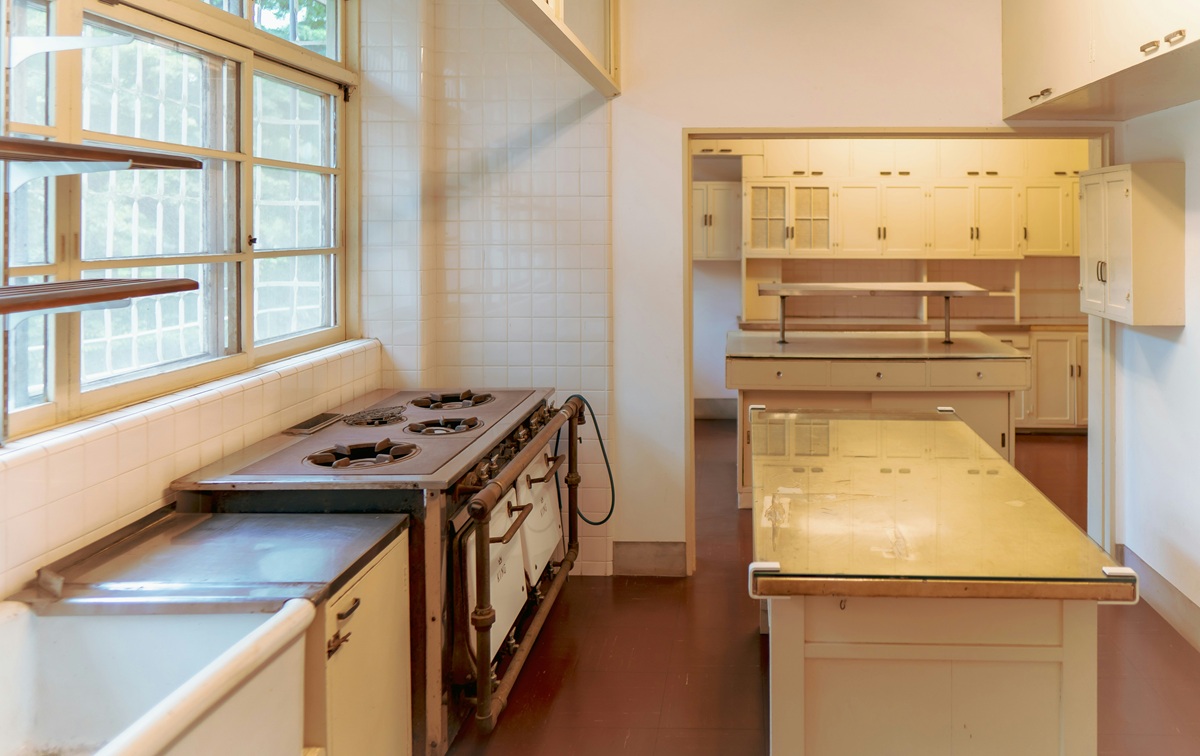 Spacious kitchen with tiled walls, vintage stoves, and yellow cabinetry.