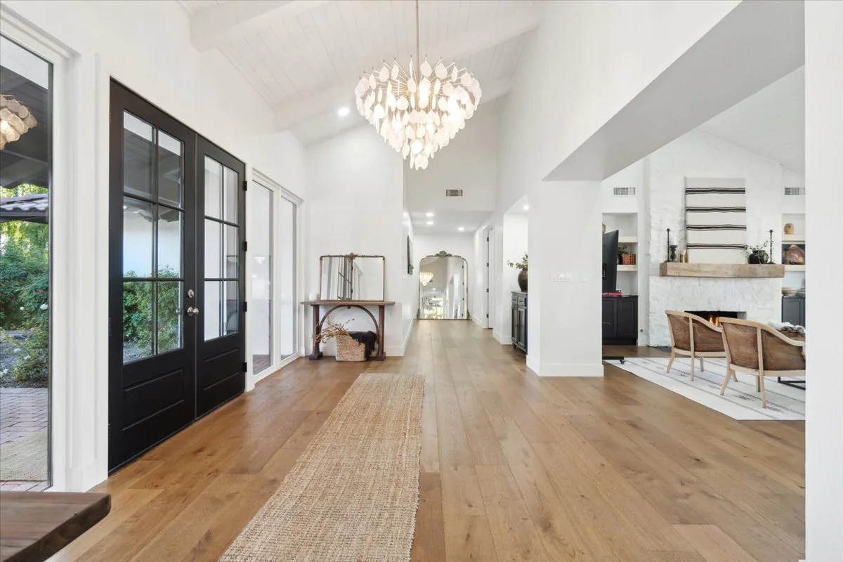 Spacious entryway with wood floors, high ceilings, and a statement chandelier leading to an open living area.
