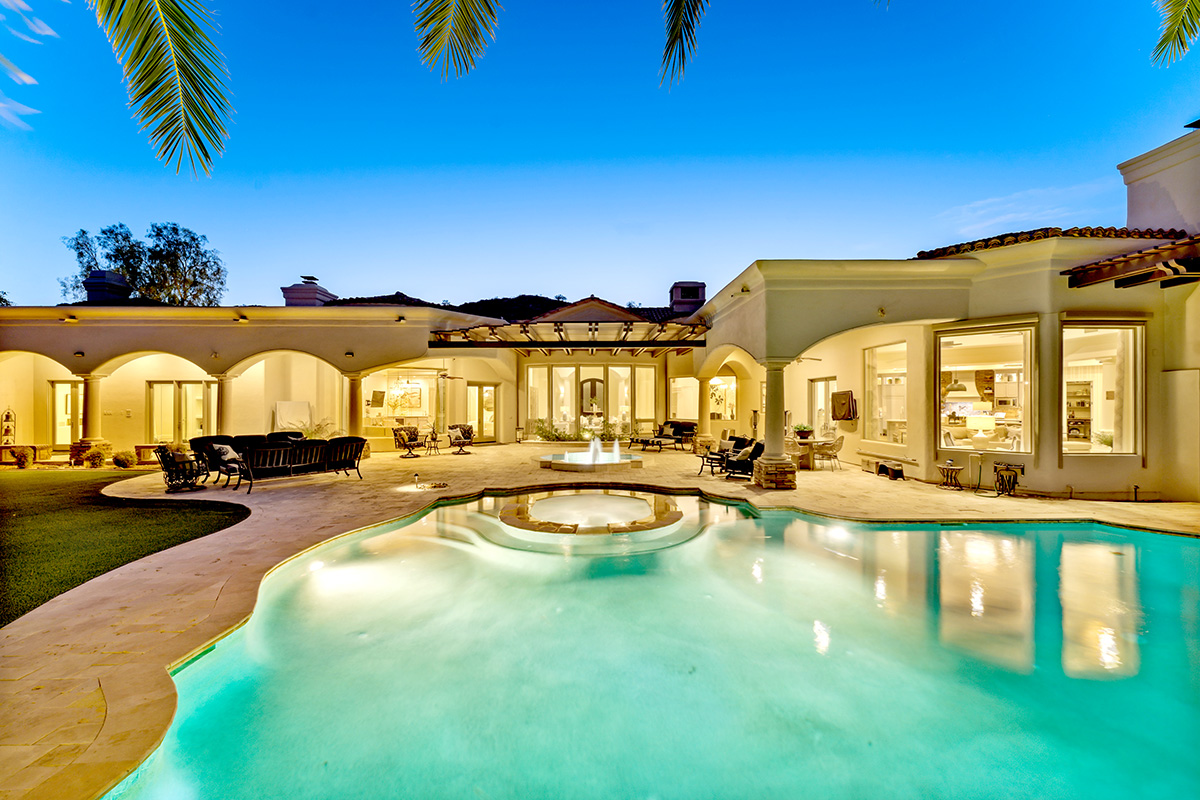 Stunning pool area of an Arizona mansion located in Paradise Valley with palm trees, outdoor seating, and a beautifully lit luxury home at twilight.