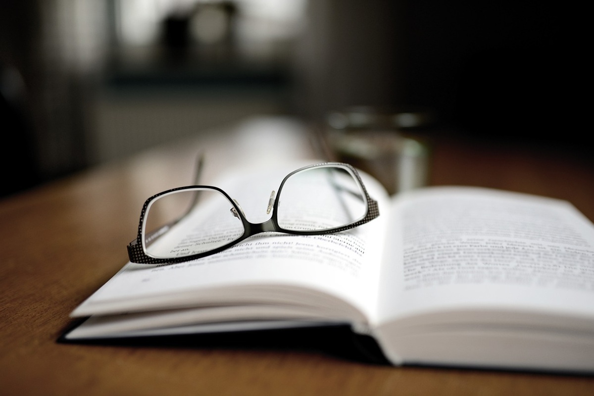 A pair of reading glasses resting on an open book, giving a sense of quiet reading or study.
