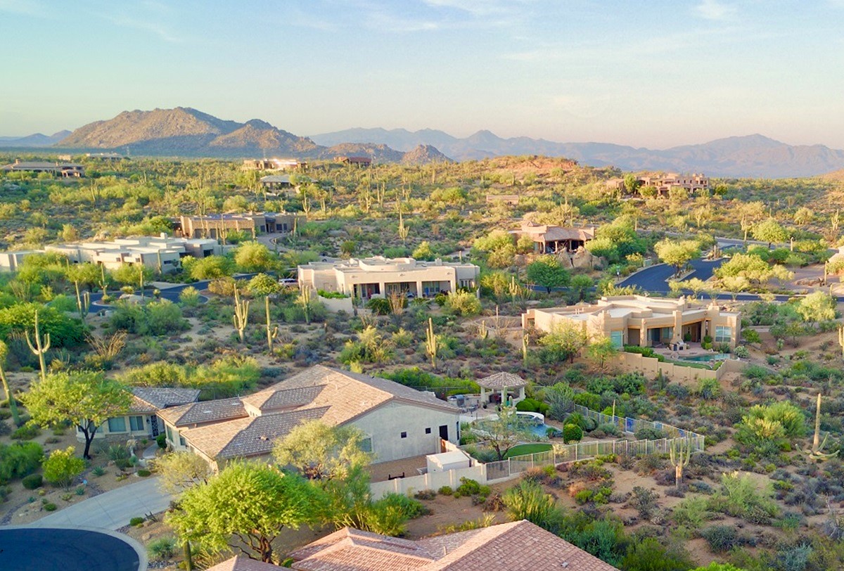 Aerial view of upscale homes nestled in Scottsdale's scenic desert landscape, surrounded by natural greenery, cacti, and distant mountains under a soft evening light.