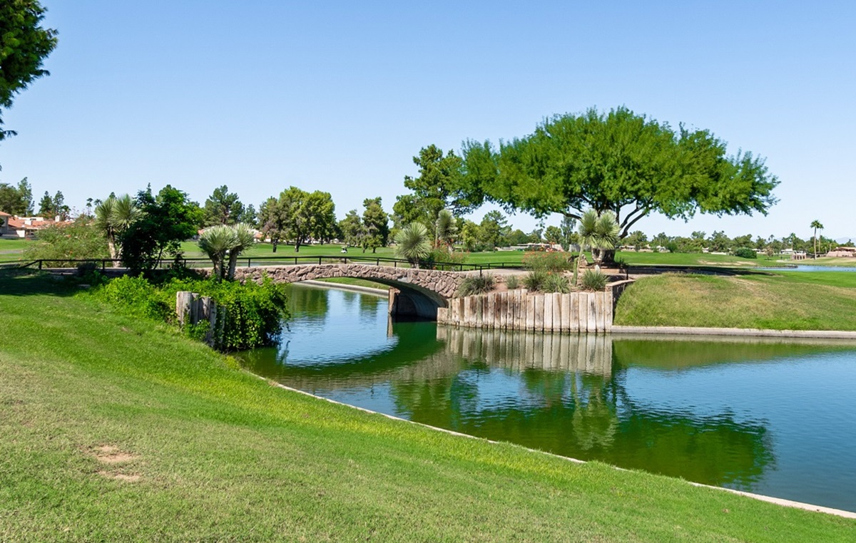 A serene golf course featuring a charming stone bridge over a small waterway, surrounded by green grass and trees on a sunny day.