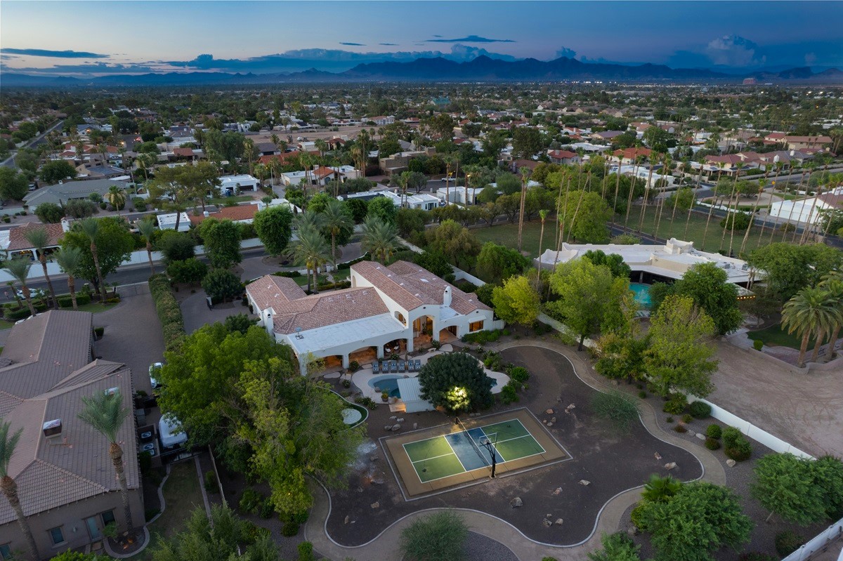 Aerial view of a spacious Scottsdale property with a tennis court, lush landscaping, and mountain views in the distance.