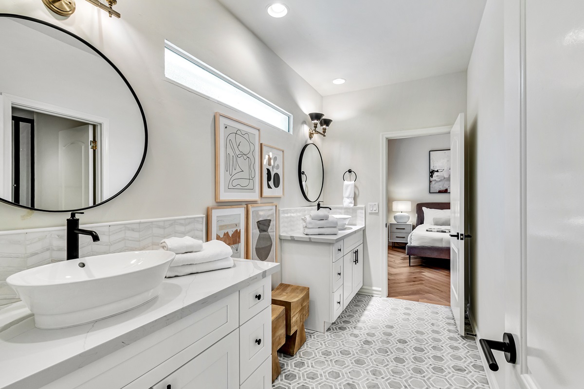 Stylish bathroom with a double vanity, circular mirrors, and contemporary decor leading into a bedroom.