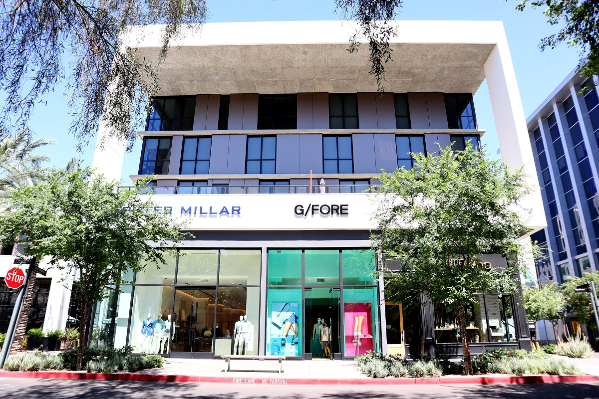 Stylish storefronts, including designer brands like Peter Millar and G/FORE, in an elegant shopping area lined with trees in Scottsdale.