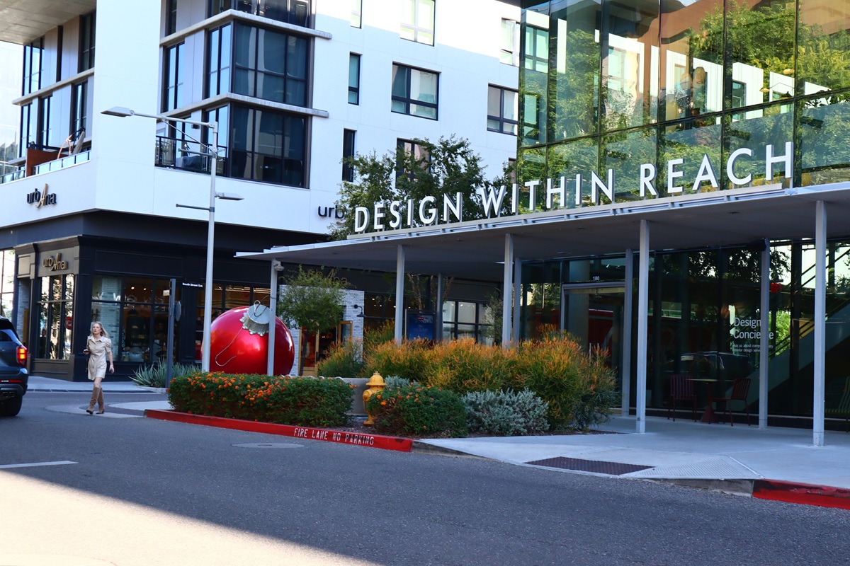 A view of Scottsdale Quarter featuring the "Design Within Reach" storefront, modern buildings with glass facades, vibrant landscaping in the background.