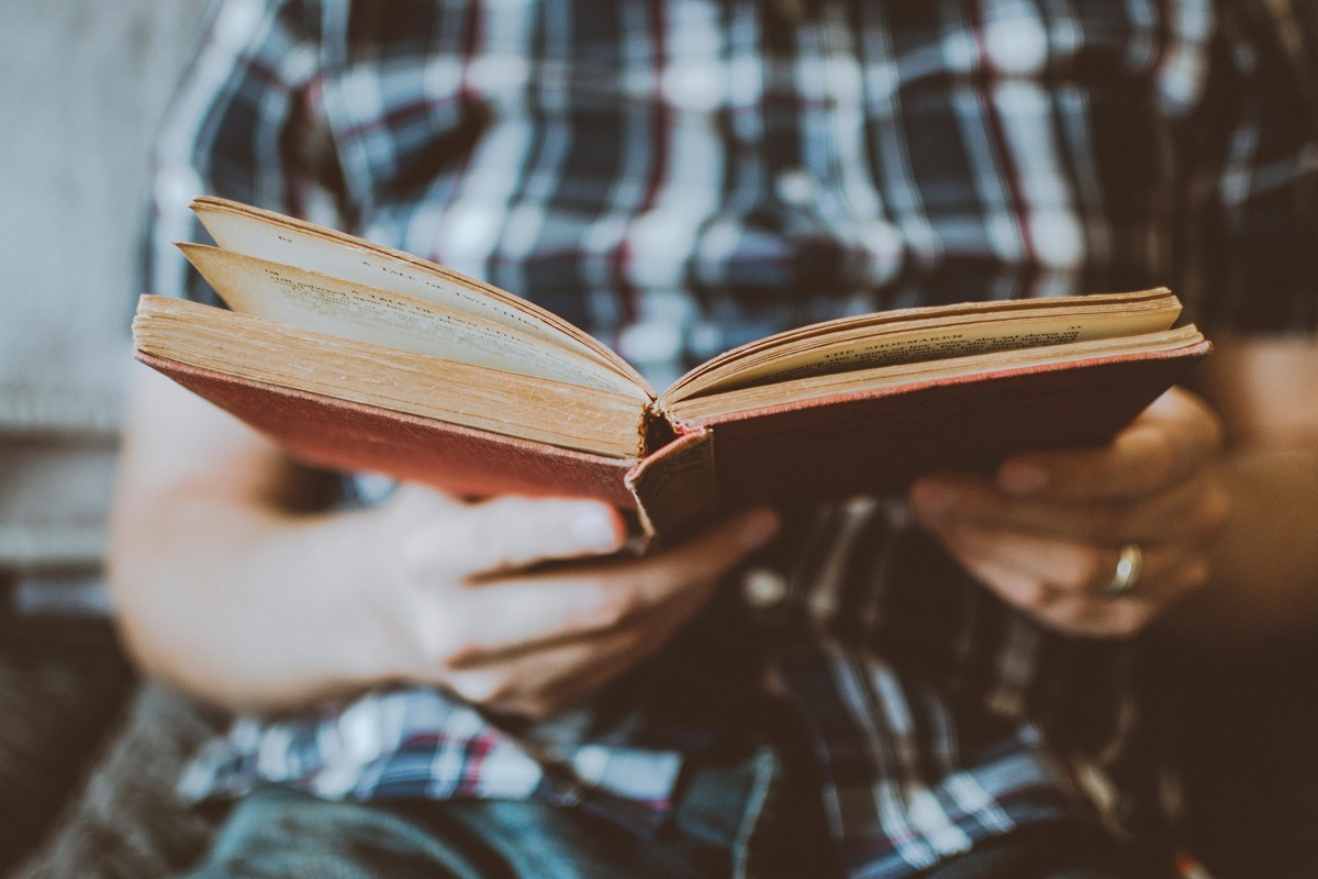 A person holding and reading an old hardcover book, sitting indoors.