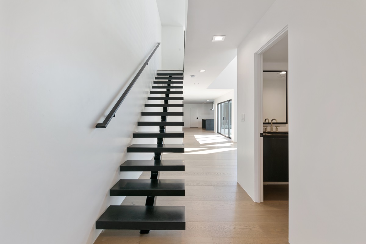 Open staircase with black floating steps and railing in a bright, minimalist townhome interior.