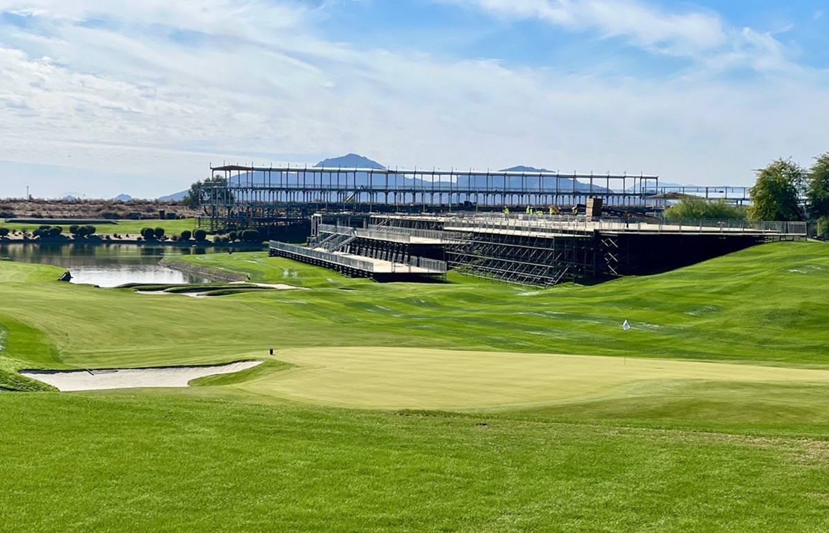 TPC Scottsdale golf course with a pond, sand traps, and construction of viewing stands, set against a mountain backdrop.