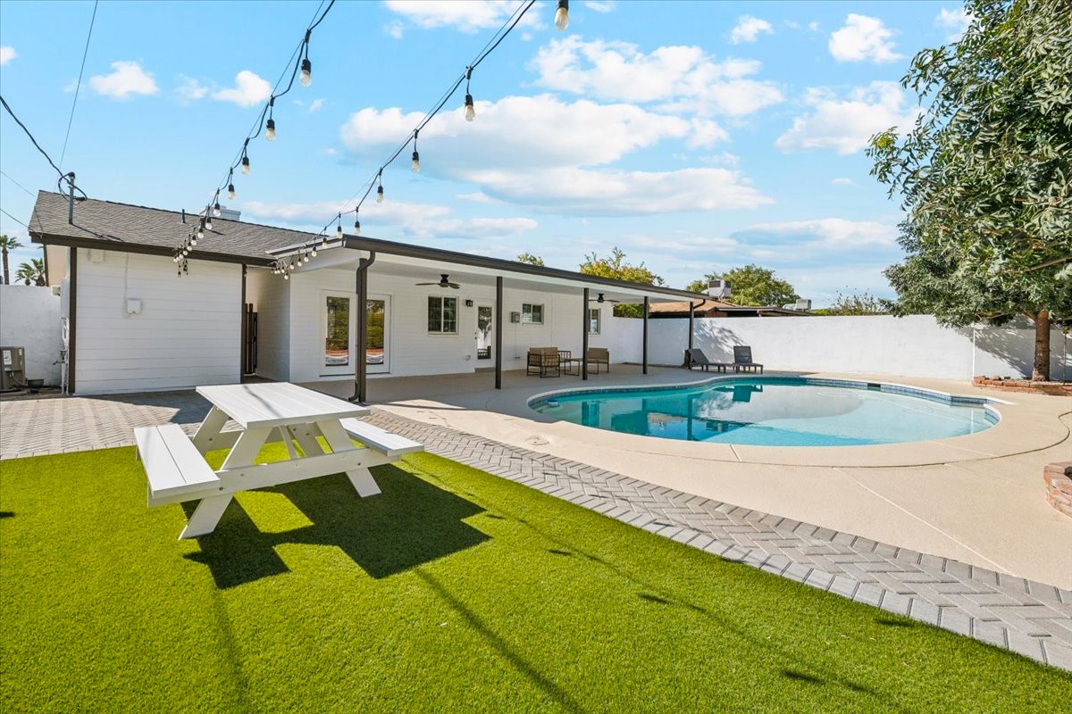 A single story home with pool seen from the backyard as a blue sky with patchy clouds fill the sky.