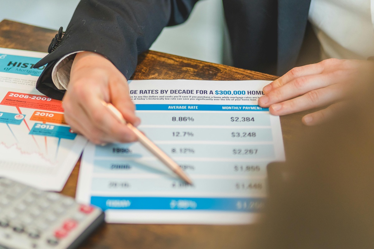Hand pointing to a table of mortgage rates and monthly payments on printed documents.