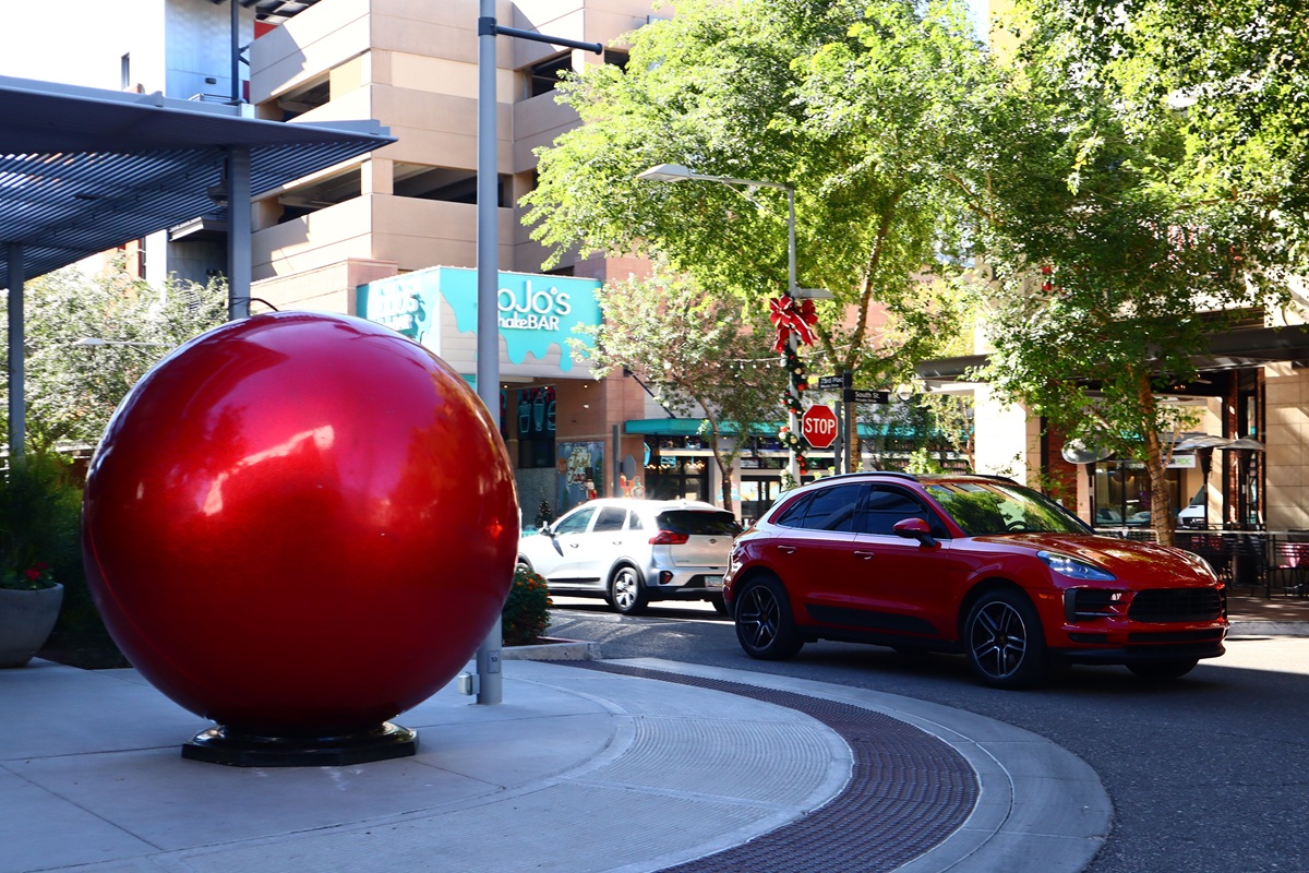 Red ornament sculpture and festive decorations at Scottsdale Quarter with cars and shops in the background.