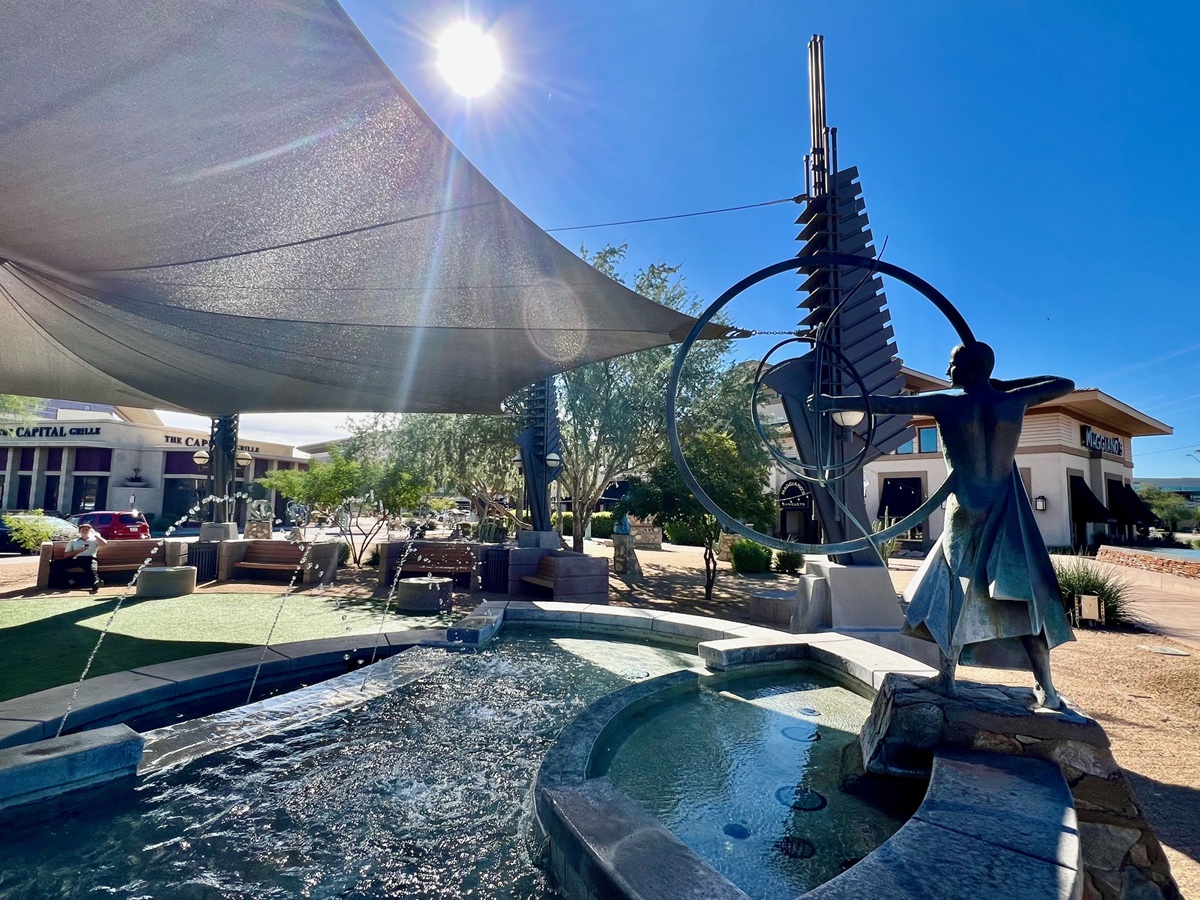 Fountain sculpture and shaded seating area at a shopping plaza in Scottsdale under a sunny sky.
