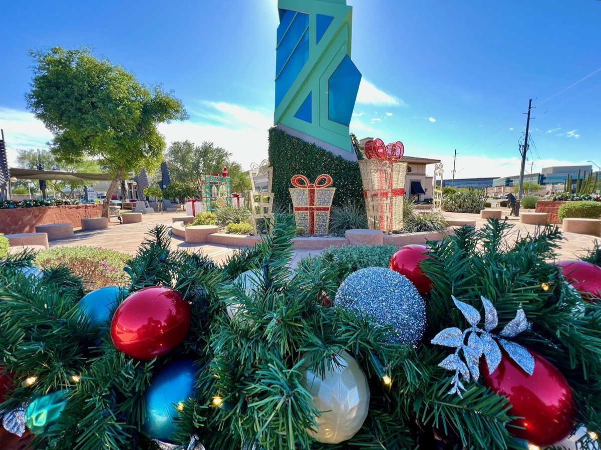 Holiday decorations near the Scottsdale Spire, featuring colorful ornaments, wrapped gift displays, and greenery under a bright sky.