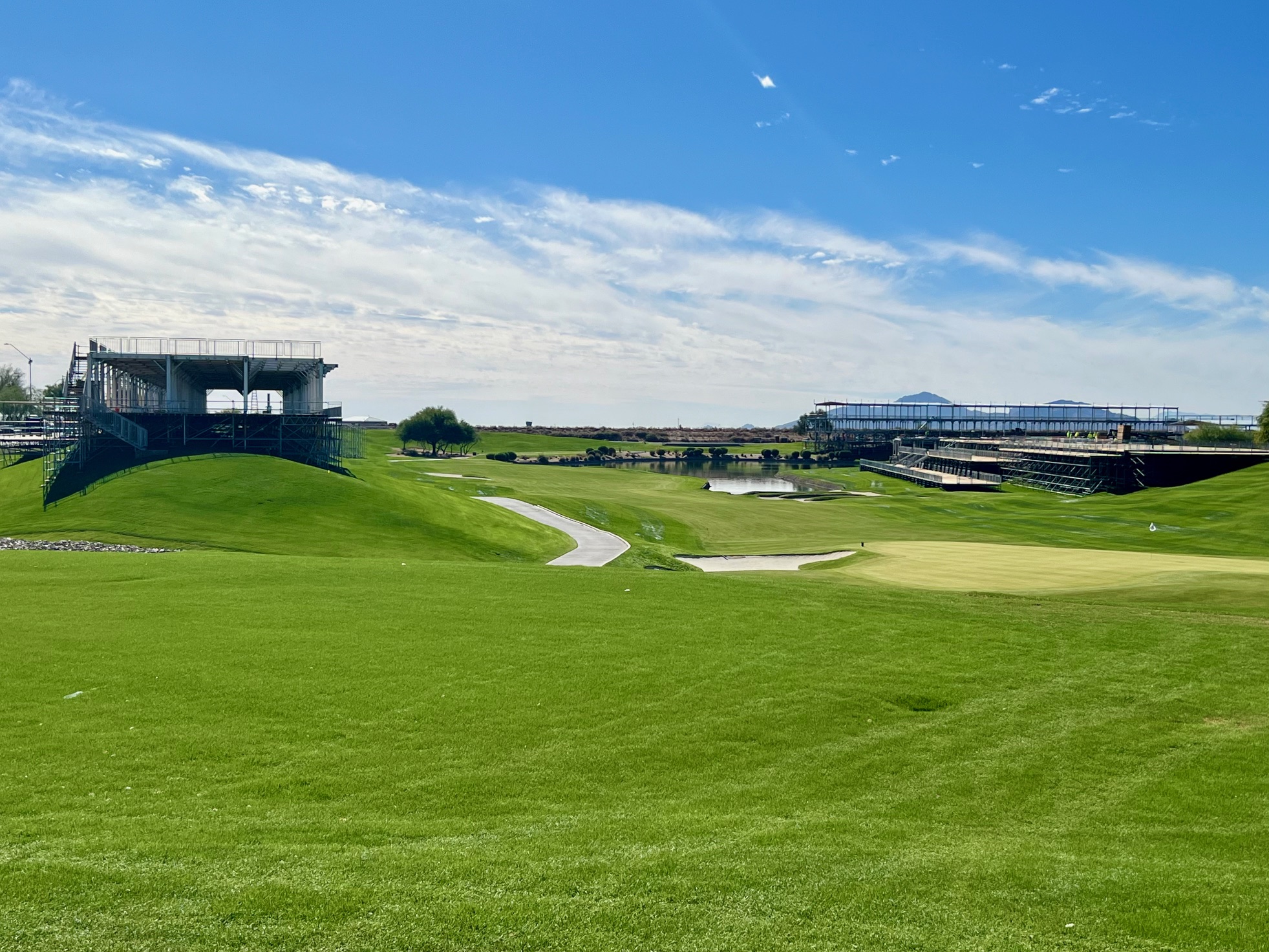 Beautiful green golf course at TPC Scottsdale with grandstands under construction for the WM Phoenix Open, under a blue sky.