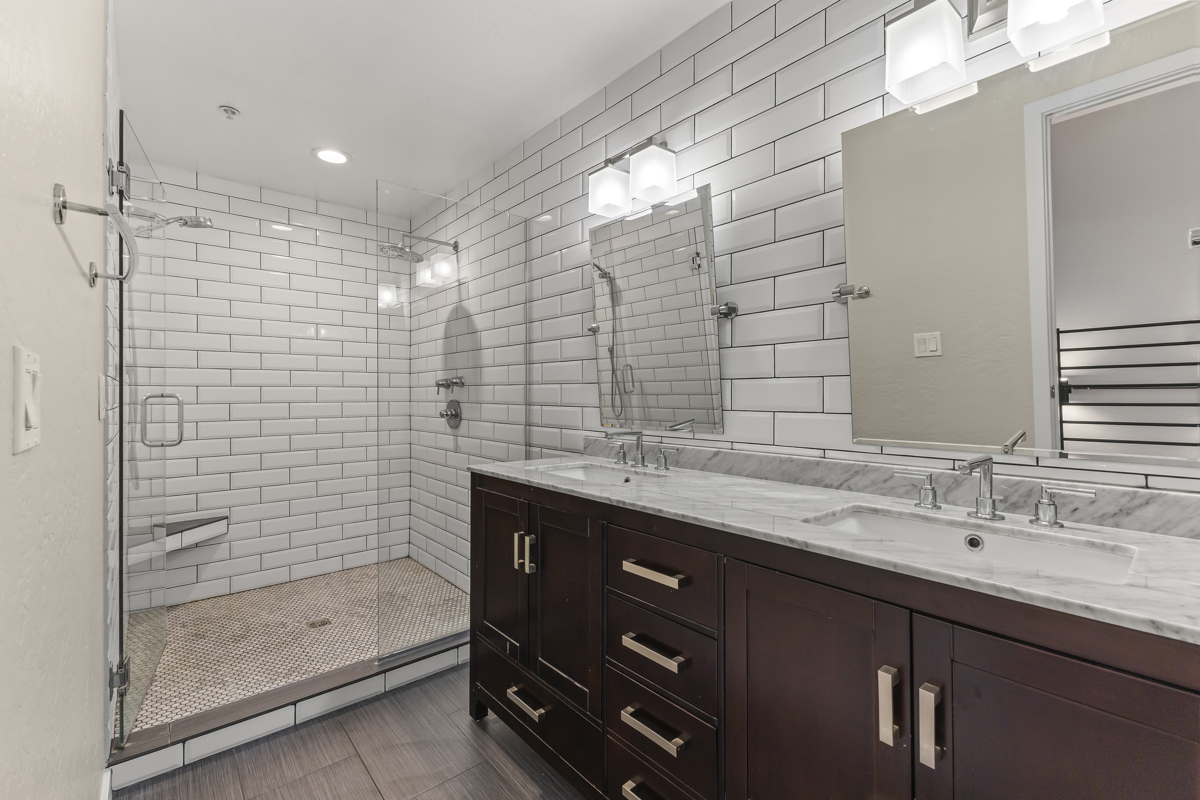 Bathroom with dual sinks, subway tiles, and walk-in shower.