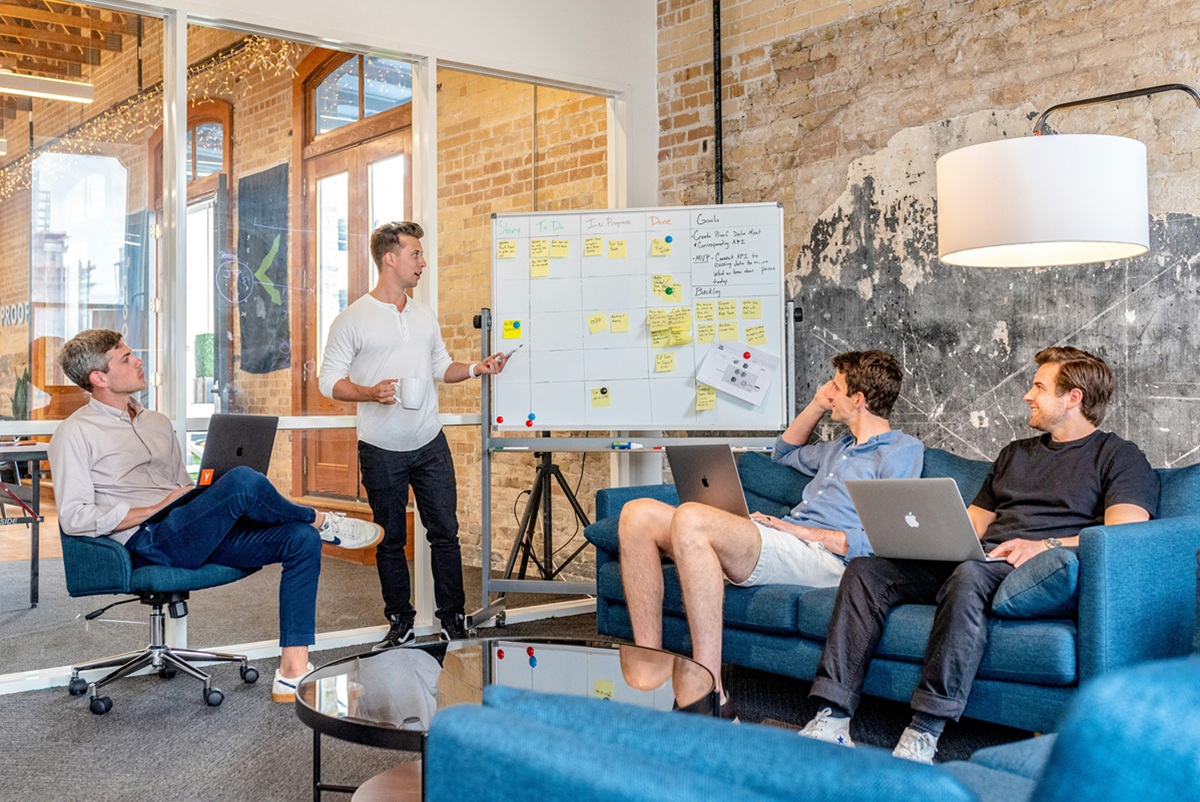 A small team of employees in a modern office discussing ideas and strategies in front of a whiteboard, showcasing brainstorming and professional development.