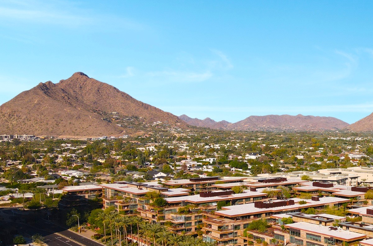 Scenic view of a sprawling residential area in Greater Phoenix, framed by mountains under a clear blue sky.