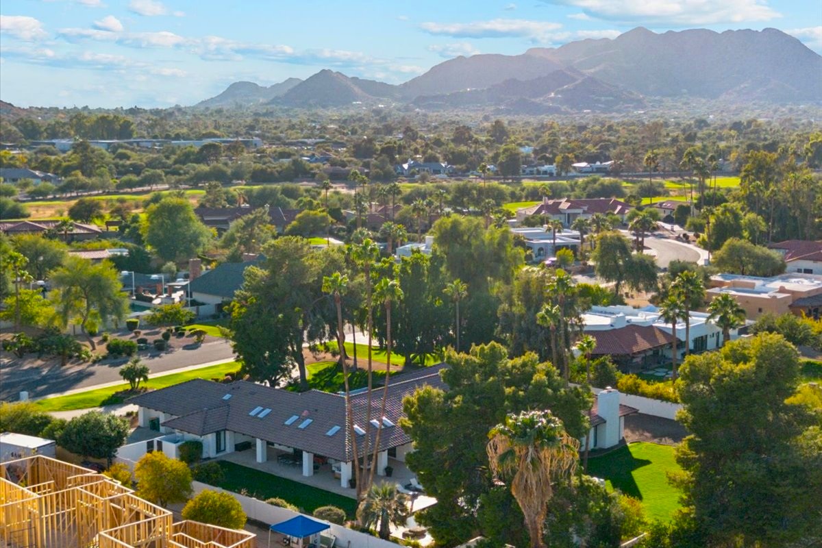 A scenic view of a suburban neighborhood in Greater Phoenix with lush greenery, palm trees, and mountains in the background under a sunny sky.