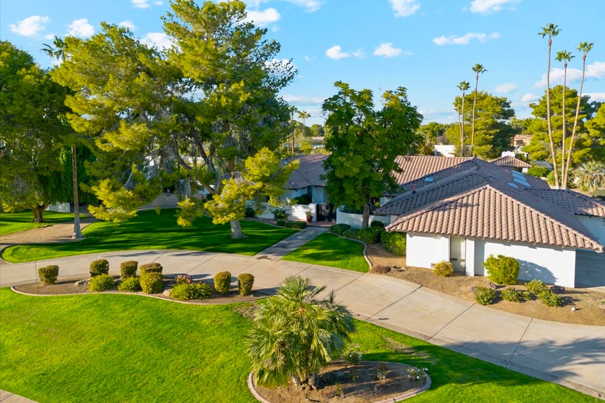 A beautiful single-story home with a tiled roof, surrounded by well-manicured lawns, trees, and a curved driveway on a sunny day.