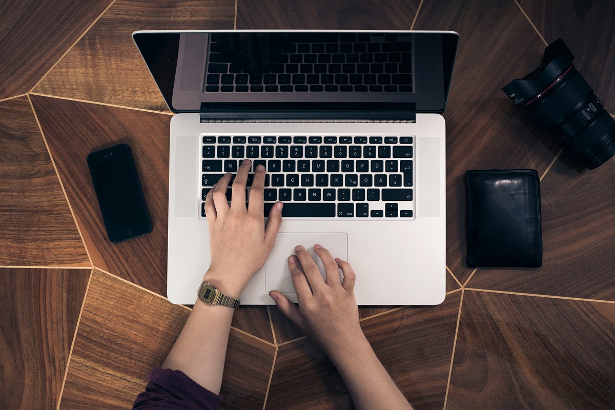 A close-up of hands typing on a laptop with a wooden desk and nearby items, symbolizing productivity and job-related tasks.