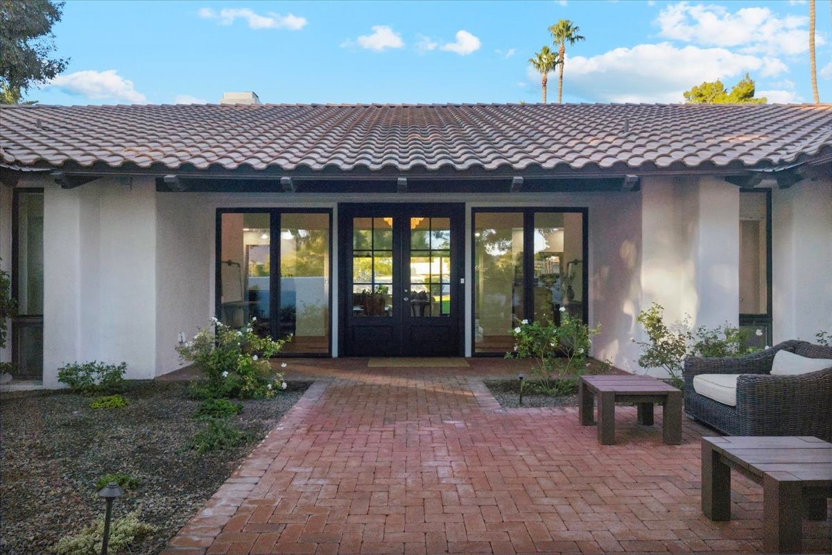 Front view of a home with a tiled roof, large glass doors, and brick patio surrounded by plants.