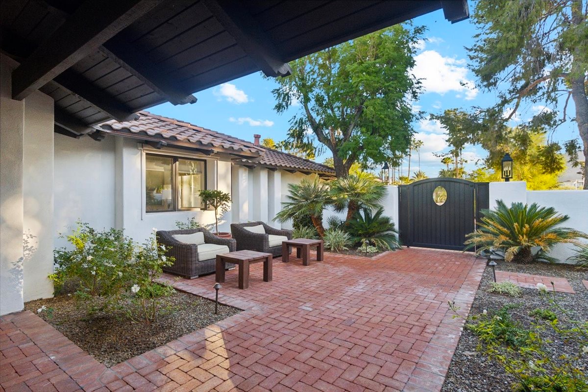 Courtyard with seating area, brick flooring, lush greenery, and a gated entrance.
