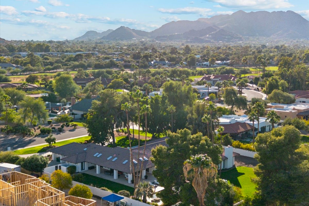 Aerial view of a lush Greater Phoenix suburb with palm trees, single-story homes, and mountains in the background.
