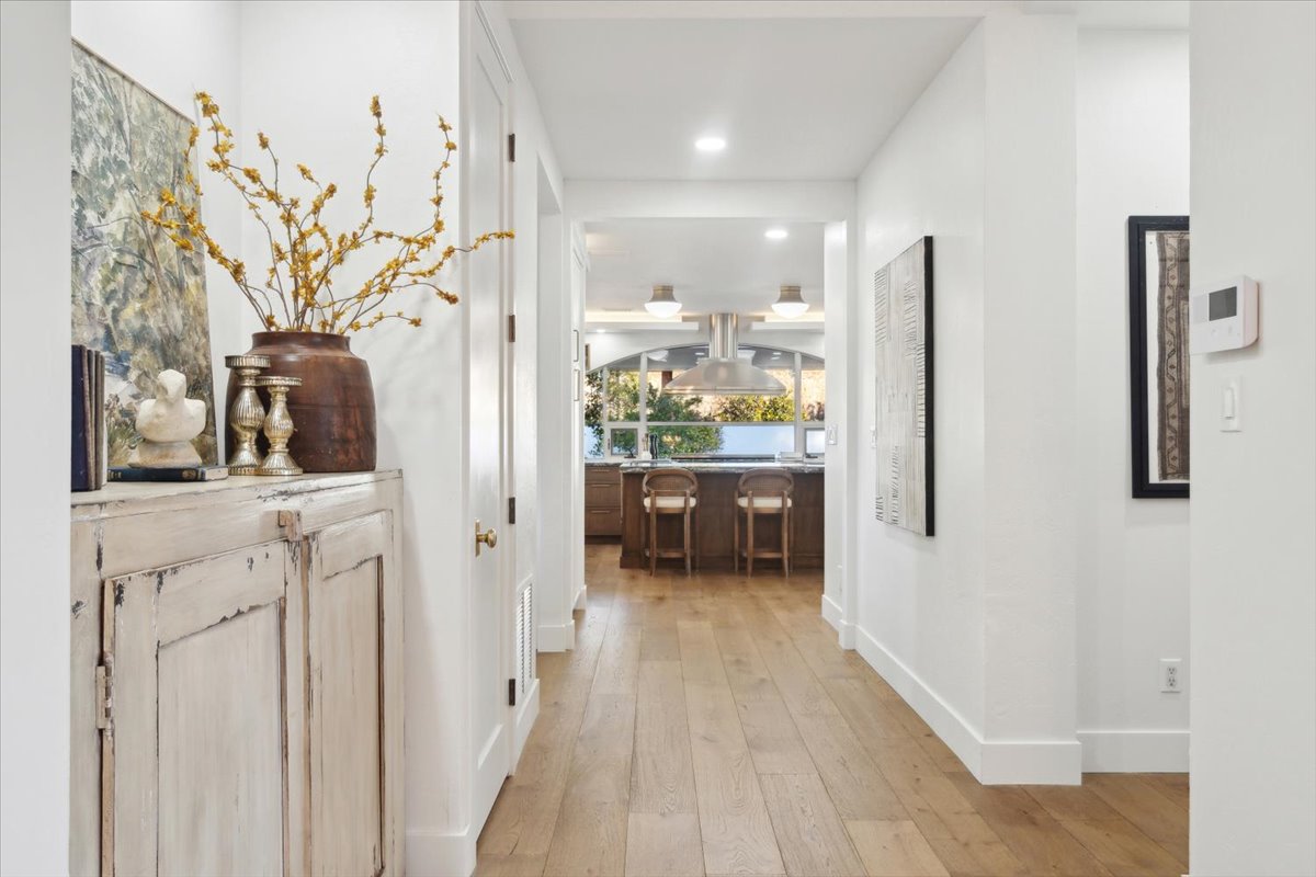 Warm hallway view into kitchen area, decorated with rustic furnishings, artwork, and floral arrangement.
