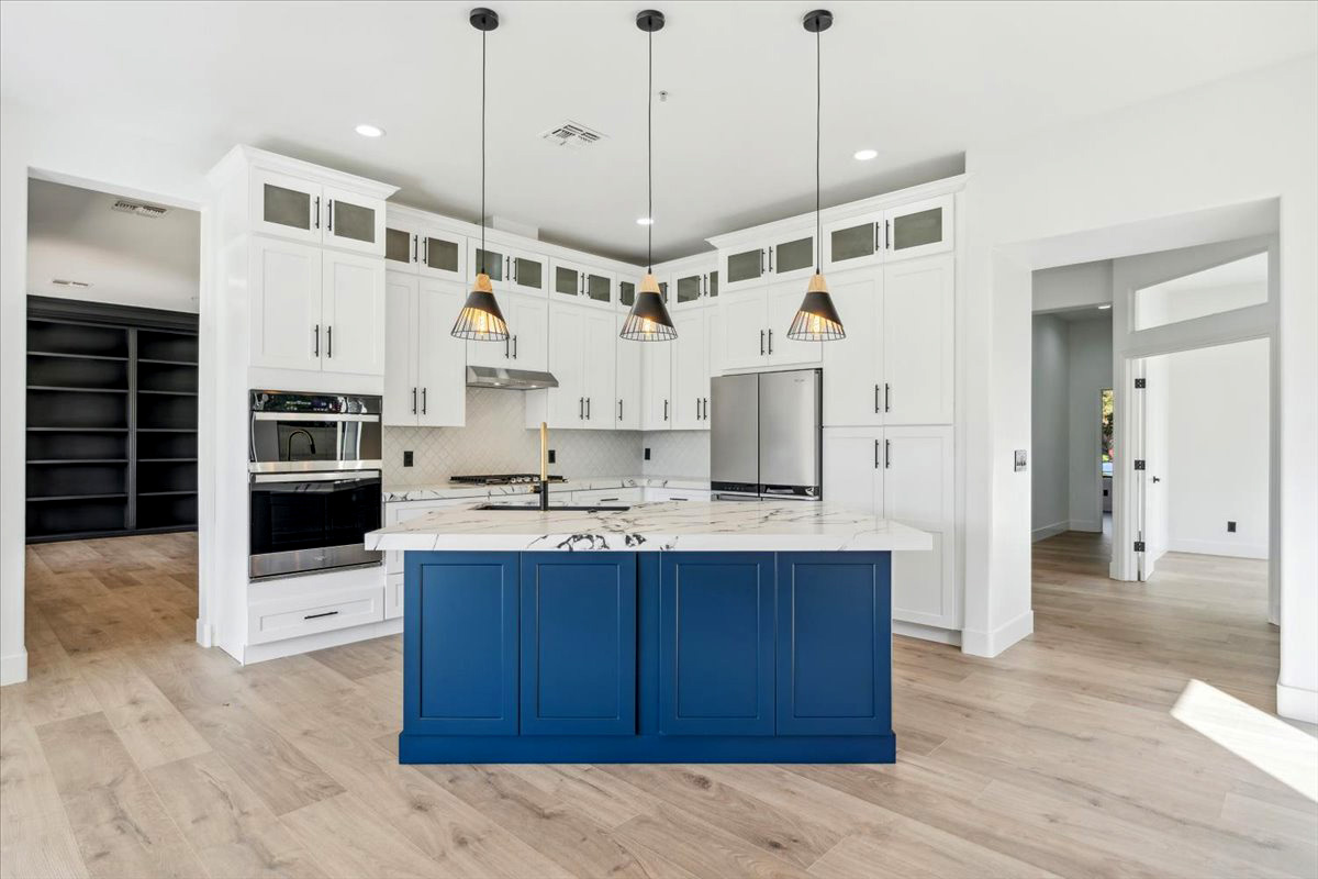 Modern kitchen with white cabinetry, a bold blue island, pendant lighting, stainless steel appliances, and light wood flooring.