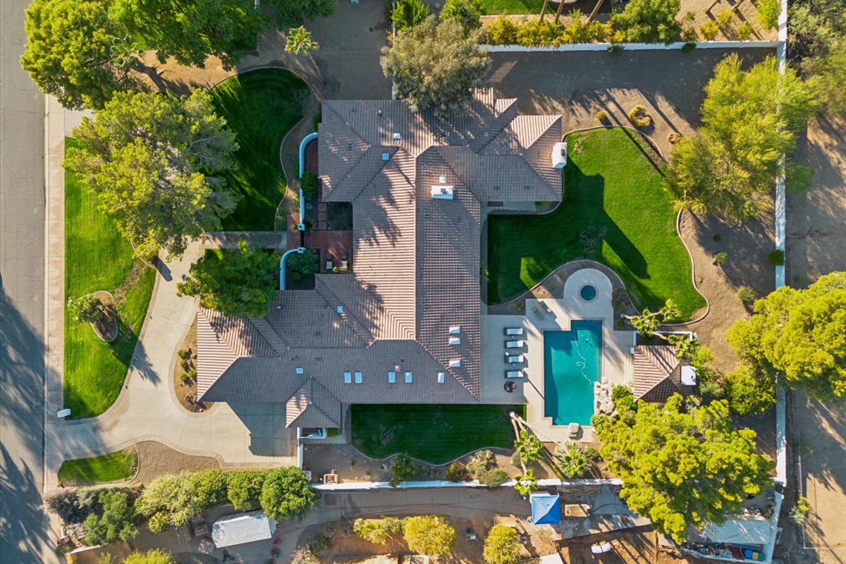 A top-down view of a sprawling luxury estate with a large pool, green lawns, and mature trees in an upscale neighborhood.