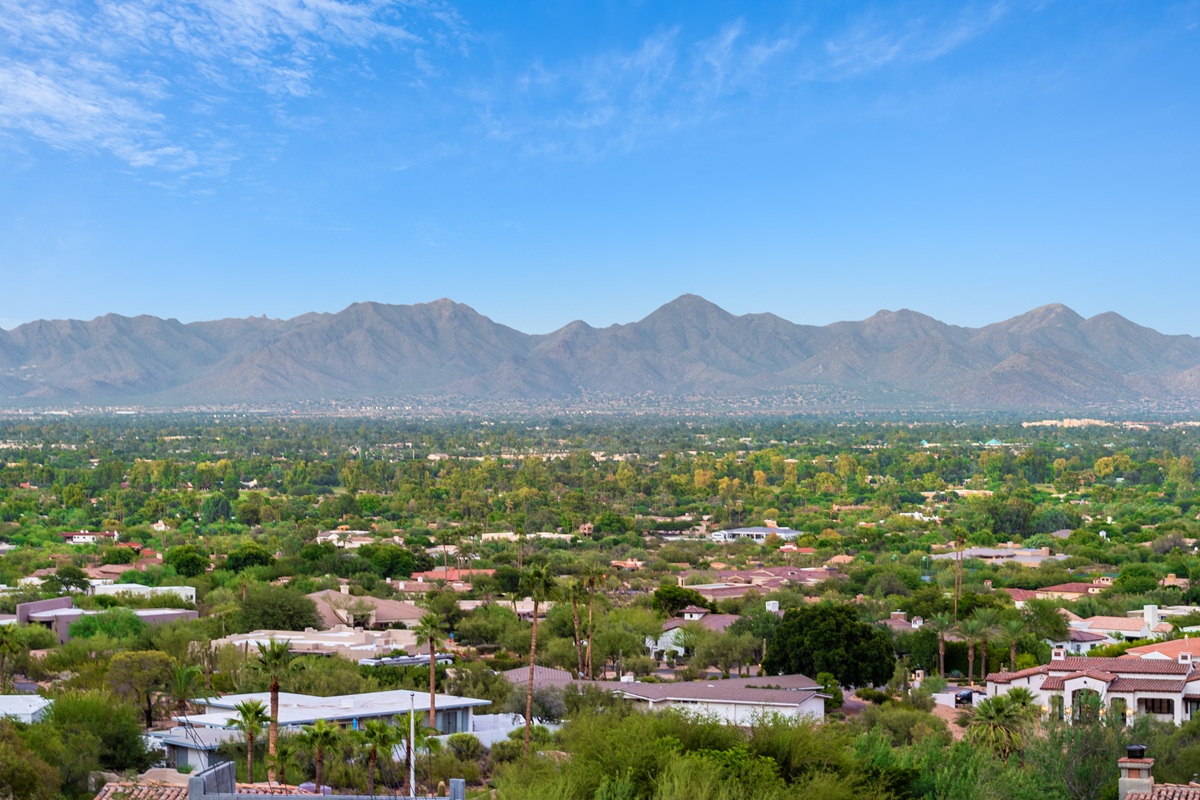 A wide view of lush Paradise Valley with scattered homes and towering desert mountains in the background under a bright blue sky.