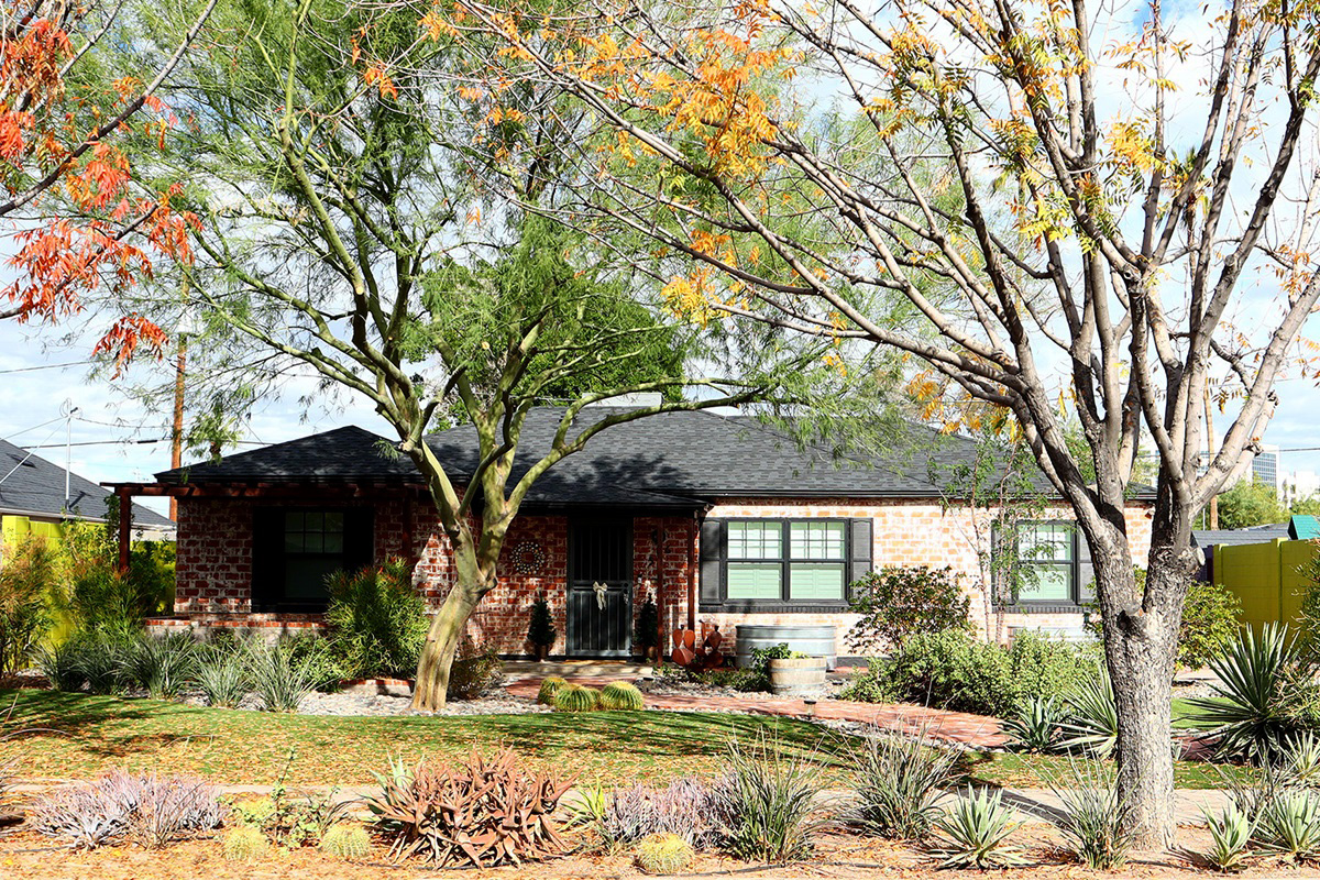 Charming brick home exterior surrounded by mature trees and desert landscaping in Phoenix.