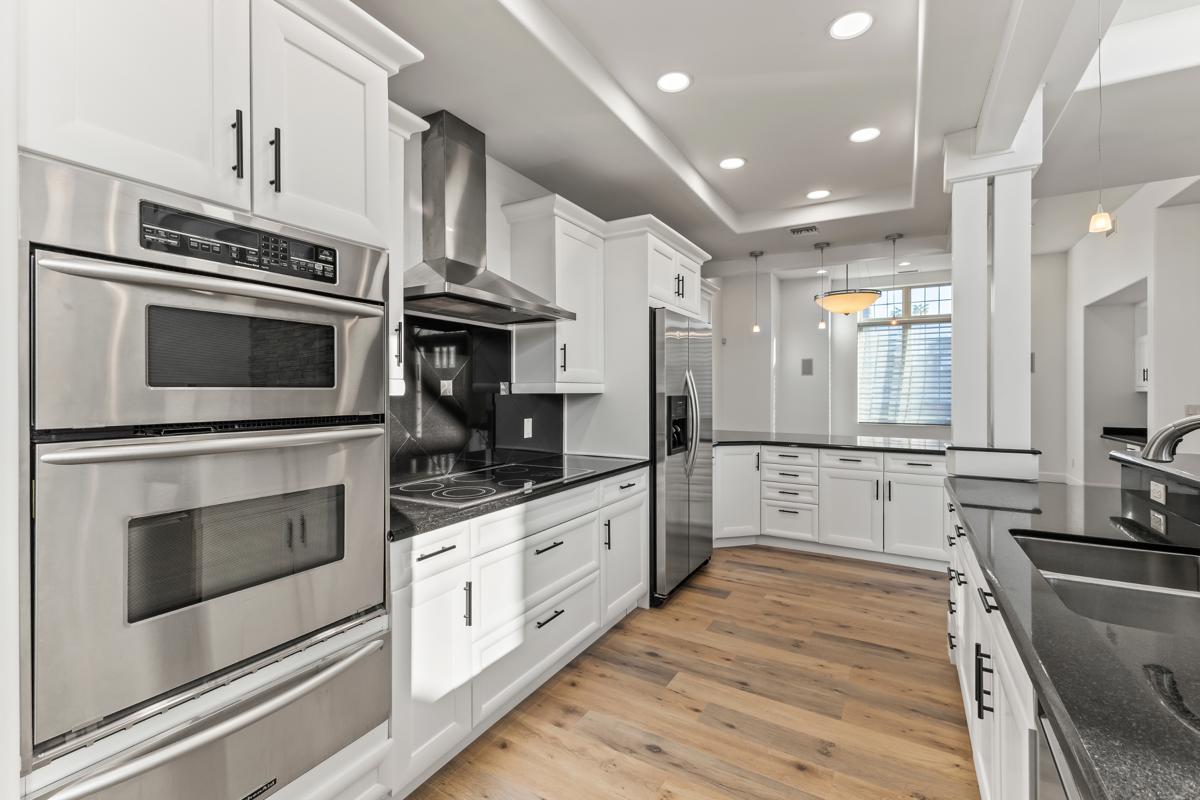Modern white kitchen with stainless appliances, black countertops, and recessed lighting.