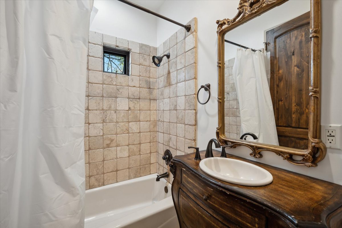 Bathroom featuring rustic wooden vanity, ornate mirror, and tiled shower with window.