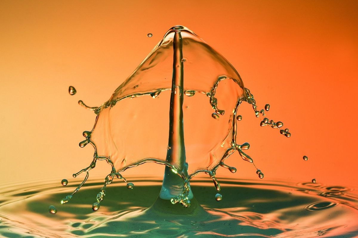 A high-speed close-up of a water splash forming a symmetrical, umbrella-like shape against an orange background.