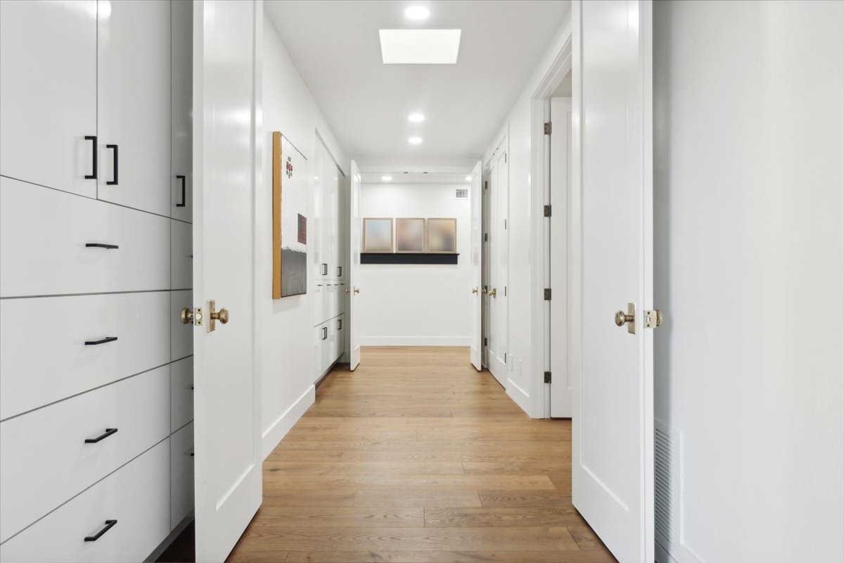 Hallway with built-in cabinets, white walls, and wood floors.