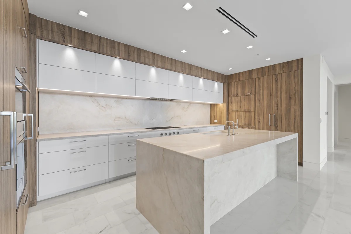 Bright gourmet kitchen with a marble waterfall island, minimalist white cabinets, integrated appliances, and warm wood paneling. Located at the Ritz-Carlton, Paradise Valley.
