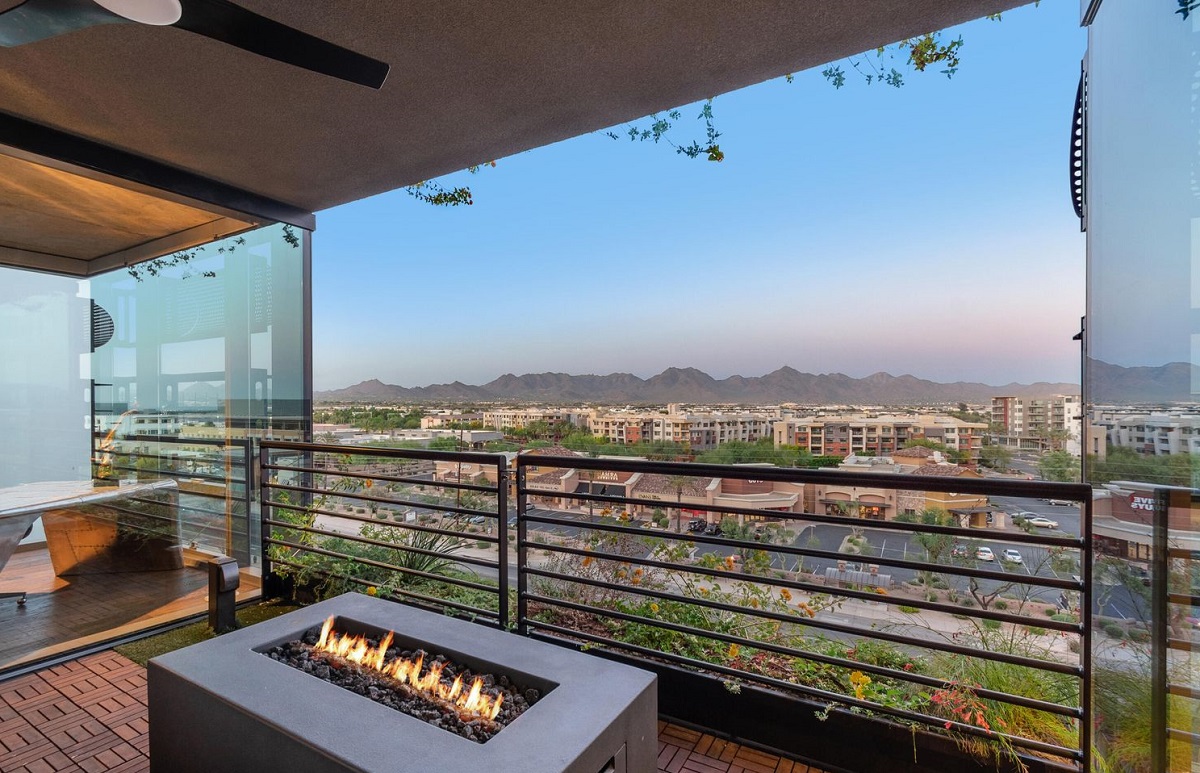 Fire pit on a private balcony overlooking city rooftops and distant desert mountains at dusk.
