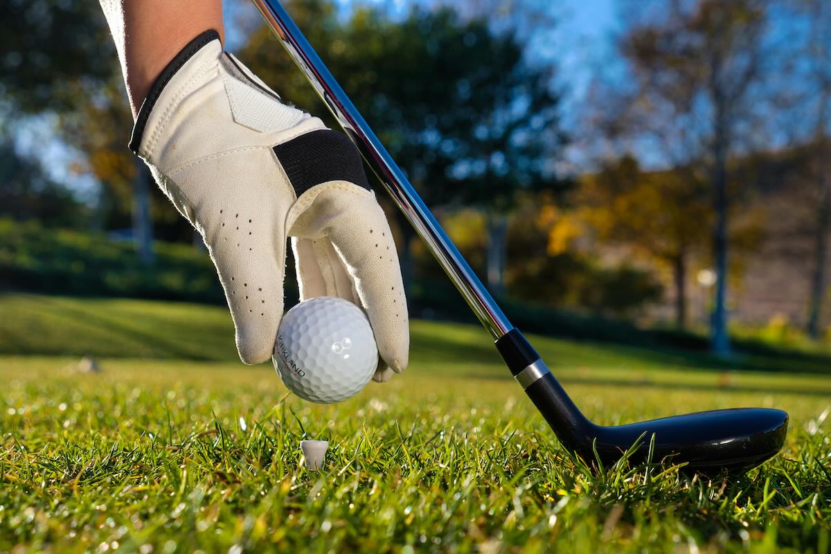 gloved hand placing golf ball on a tee