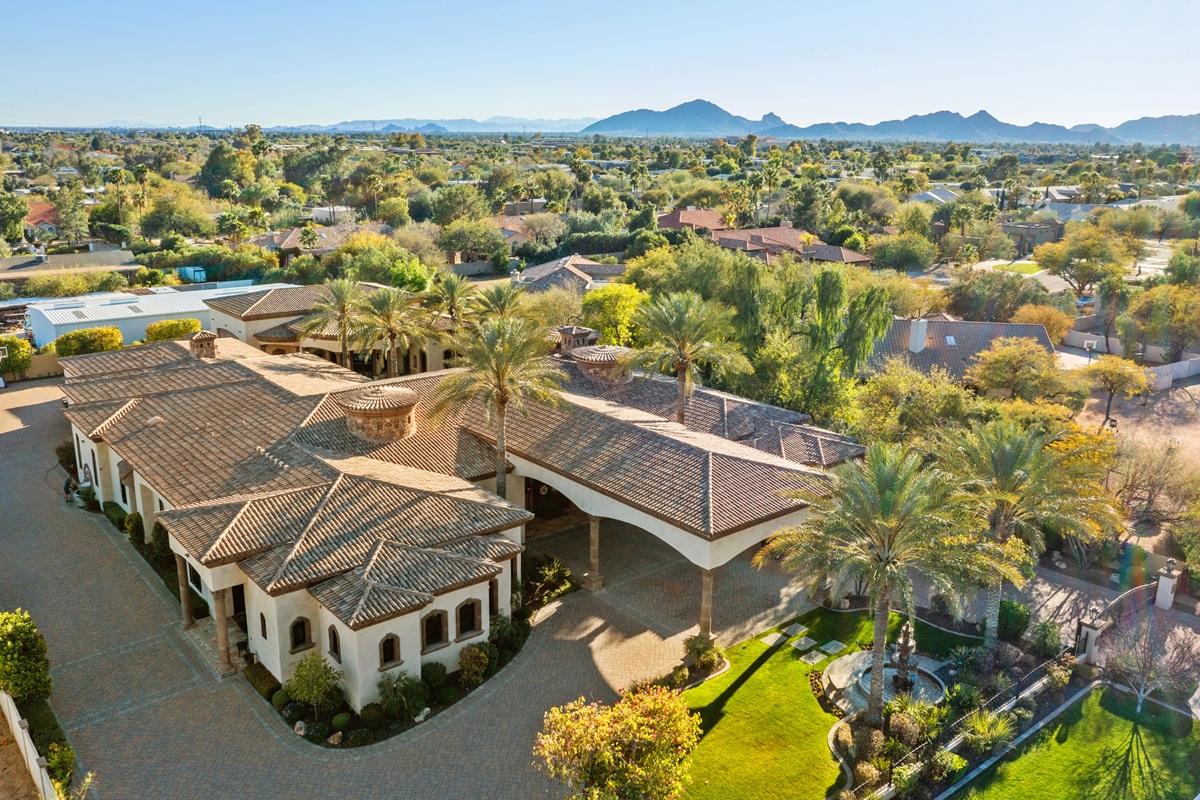 Aerial view of estate with tile roof, palm trees, and mountain backdrop.
